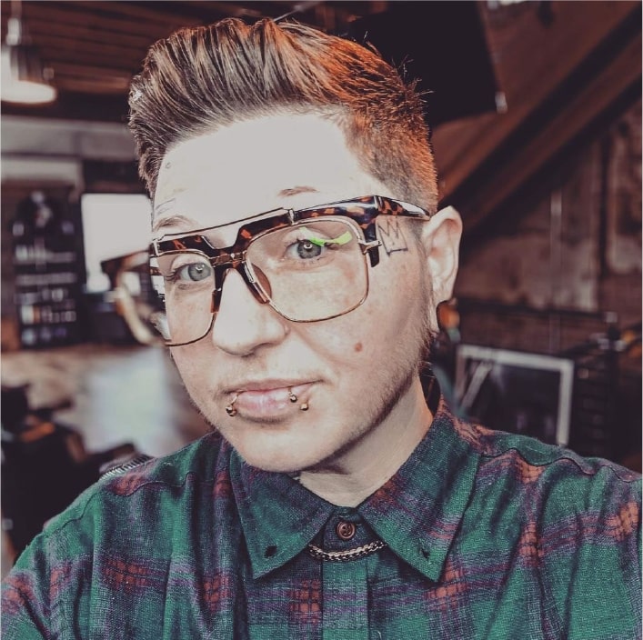 person with short haircut, glasses and lip rings