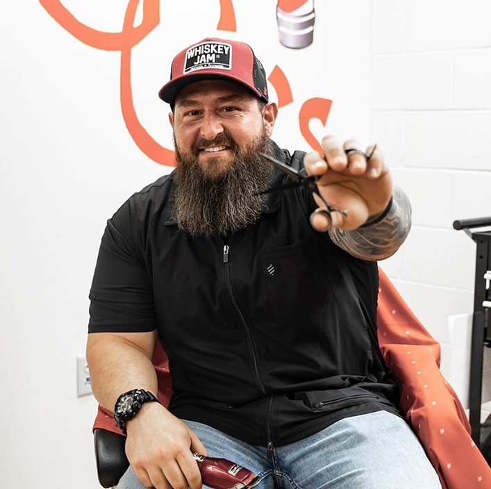 guy with beard sitting holding out shears