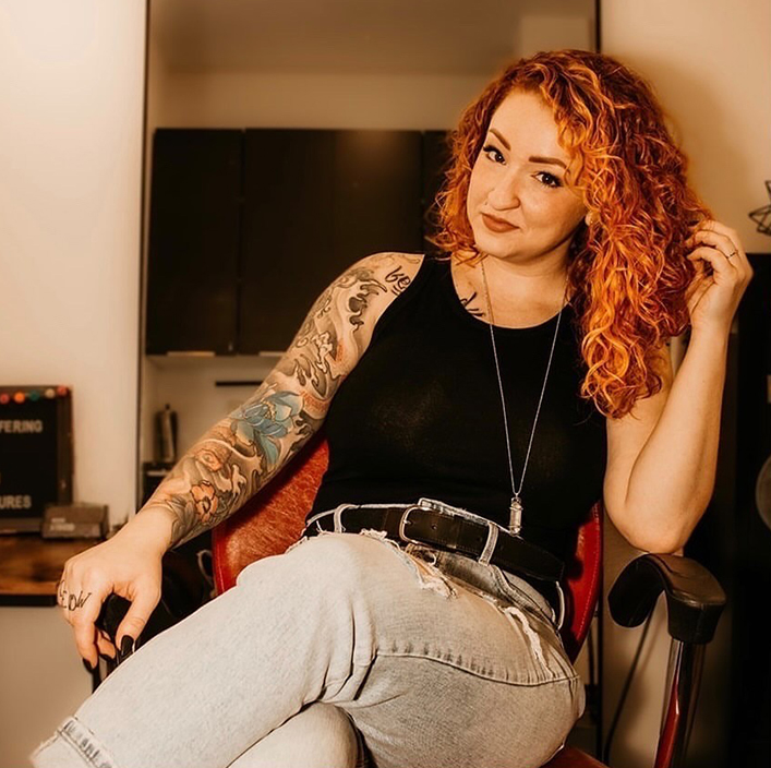 woman with tattooed arm and curly hair sitting in chair