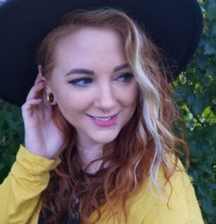 woman with hat on red hair with blonde streak and nose piercing in yellow shirt